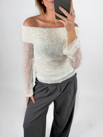 Modelfoto af pige i cremefarvet MAISY off-shoulder blondebluse og grå LISA bukser. Alt er fra BySofieSønderby.