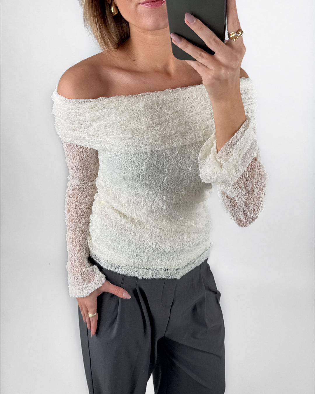 Modelfoto af pige i cremefarvet MAISY off-shoulder blondebluse og grå LISA bukser. Alt er fra BySofieSønderby.