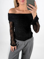 Modelfoto af pige i sort MAISY off-shoulder blondebluse og grå LISA bukser. Alt er fra BySofieSønderby.