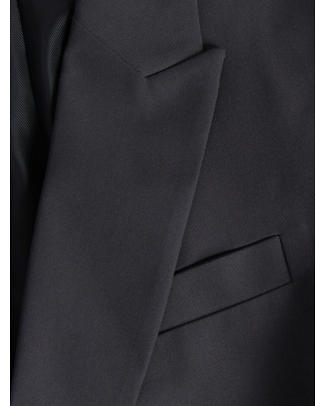En mørk jakke med en klap over brystlommen. Stoffet er glat og elegant i et formelt design.
