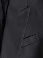 En mørk jakke med en klap over brystlommen. Stoffet er glat og elegant i et formelt design.