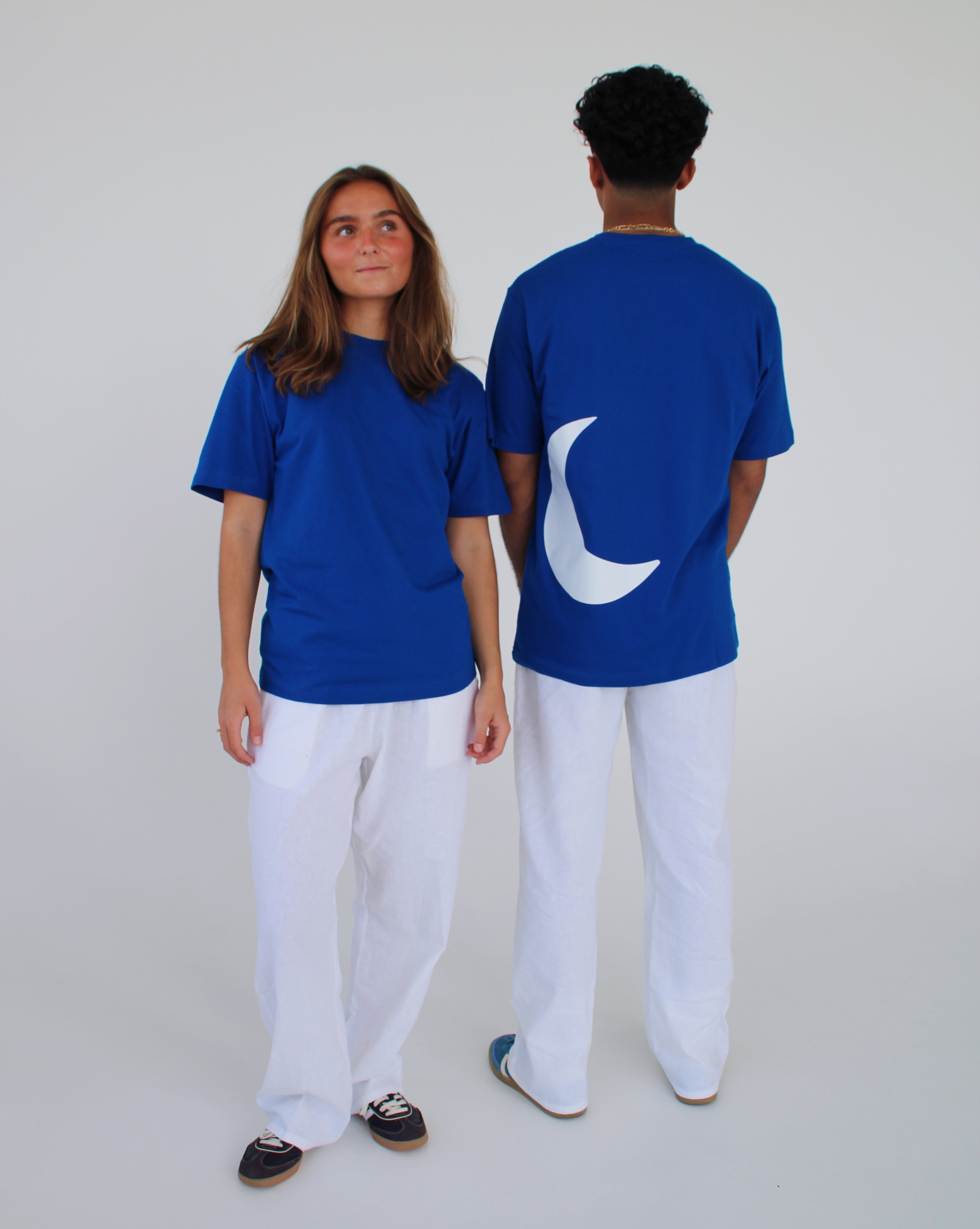 To personer iført blå T-shirts, en vender fremad og en med en halvmåne på ryggen, i et lyst rum iført hvide bukser.