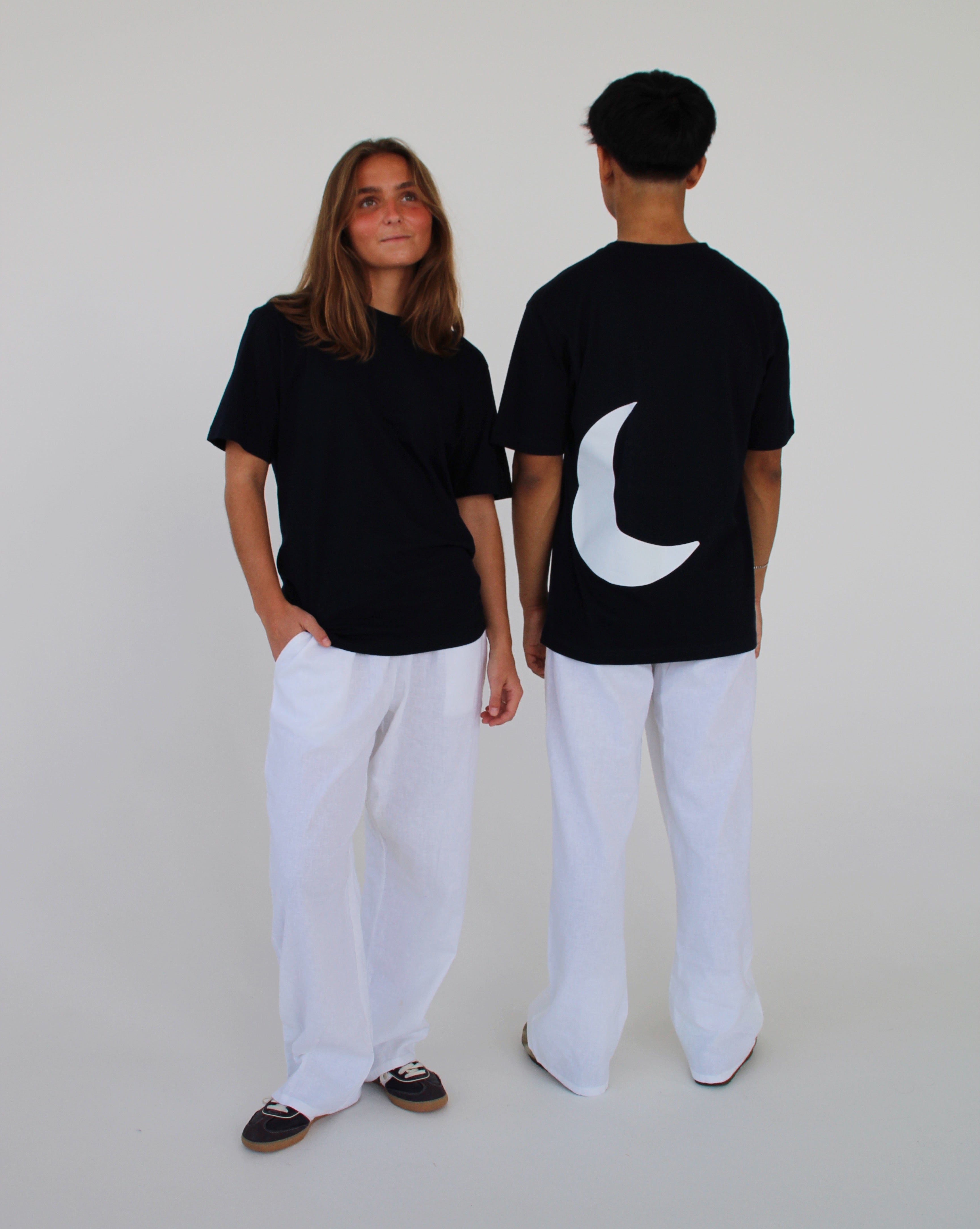 To personer iført sorte T-shirts og hvide bukser står i et hvidt rum; den ene er vendt mod kameraet, mens den anden viser en hvid halvmåne på ryggen.
