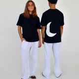 To personer i sorte t-shirts og hvide bukser står sammen; den ene vender mod kameraet, den anden med ryggen til. T-shirten har en stor hvid halvmåne bagpå.