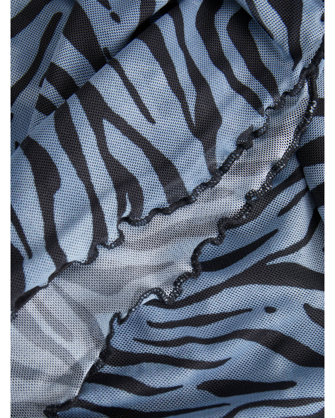 Stofdetalje med sort-zebradesign på lyseblå baggrund. Materialet er foldet, hvilket skaber en bølget kant, der giver en tekstureret og dynamisk effekt i nærbilledet.