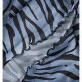 Stofdetalje med sort-zebradesign på lyseblå baggrund. Materialet er foldet, hvilket skaber en bølget kant, der giver en tekstureret og dynamisk effekt i nærbilledet.