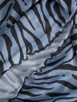 Stofdetalje med sort-zebradesign på lyseblå baggrund. Materialet er foldet, hvilket skaber en bølget kant, der giver en tekstureret og dynamisk effekt i nærbilledet.