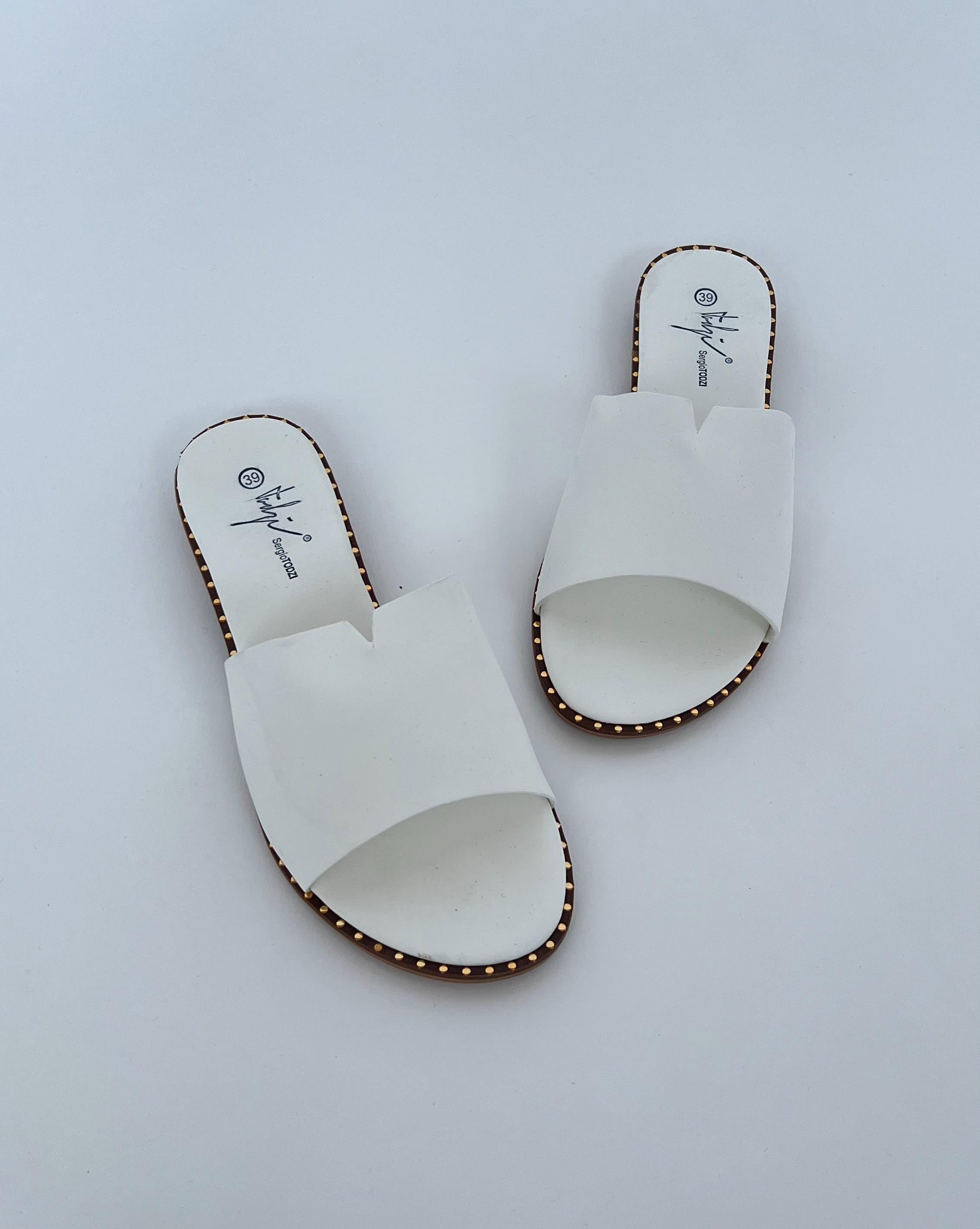 Hvide sandaler med brede stropper ligger stille på en hvid overflade. Indersålen har teksten "ByJinji Signature, EU 39".