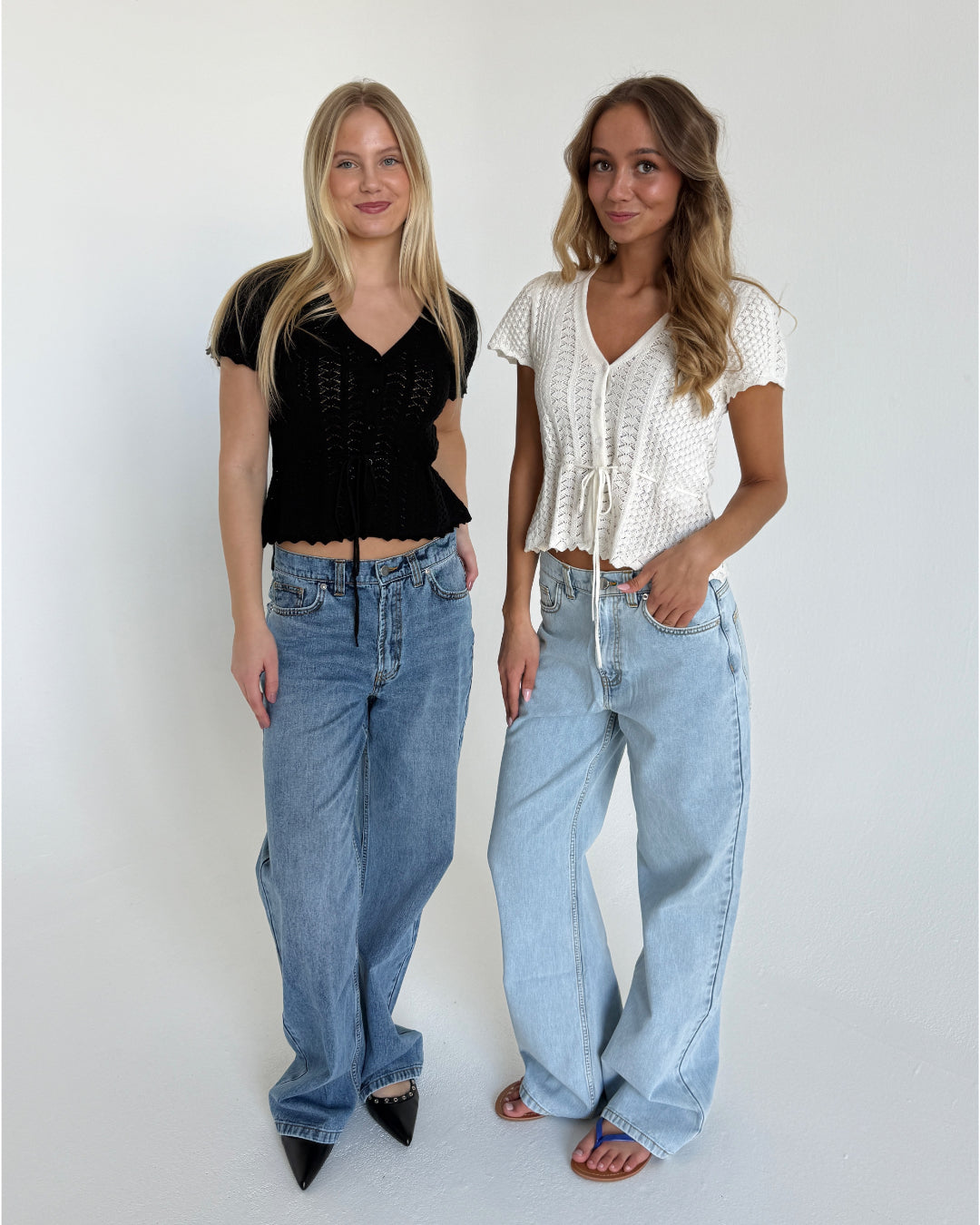 Modelfoto af to piger. Den en bærer en sort top og blå jeans, den anden pige bærer en hvid top og blå Nanna jeans. Alt fra BySofieSønderby.