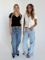 Modelfoto af to piger. Den en bærer en sort top og blå jeans, den anden pige bærer en hvid top og blå Nanna jeans. Alt fra BySofieSønderby.