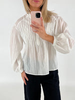 En person i en hvid bluse tager et billede med en mobiltelefon med lyserødt cover i et minimalistisk, lyst rum.
