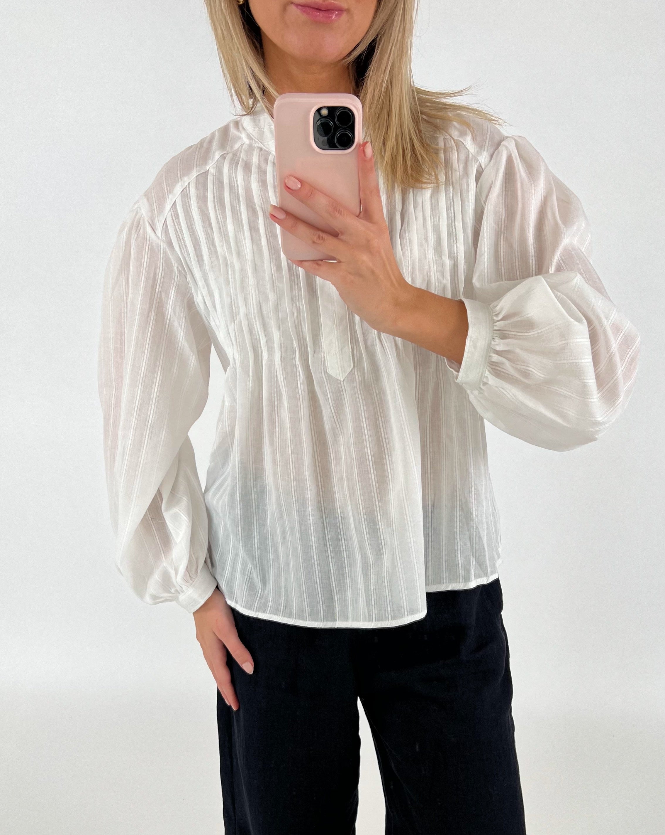 En person i en hvid bluse tager et billede med en mobiltelefon med lyserødt cover i et minimalistisk, lyst rum.
