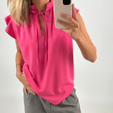 En person iført en pink bluse tager et billede med en smartphone. Personen står oprejst og befinder sig i et neutralt, lys miljø.