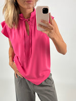 En person iført en pink bluse tager et billede med en smartphone. Personen står oprejst og befinder sig i et neutralt, lys miljø.