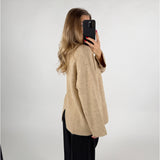 Kvinde iført beige sweater og sorte bukser, tager et spejlbillede med sin telefon. Hun står i en lys, minimalistisk indretning.