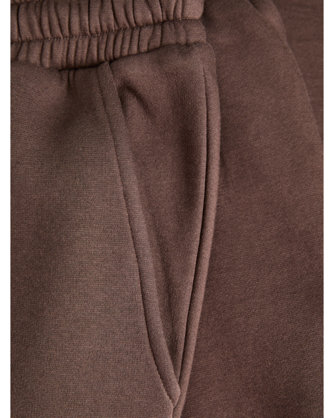 Brune joggebukser med elastisk linning og en lomme. Stoffet ser blødt og komfortabelt ud.