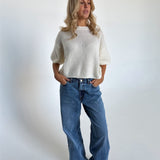 Modelfoto af pige i hvid Poppy strik t-shirt og blå Nanna jeans. Alt er fra BySofieSønderby