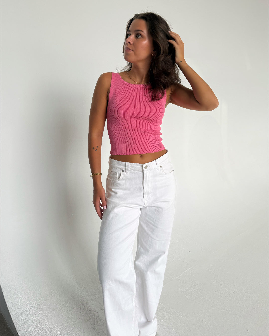 Modelfoto af pige som bærer en Posie top i pink, samt et par hvide Nanna jeans. Baggrund hvid. Alt fra By Sofie Sønderby