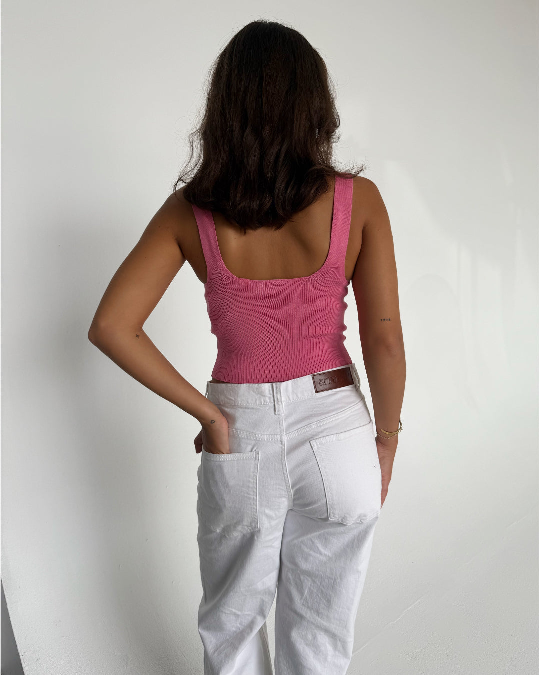 Modelfoto af pige som bærer en Posie top i pink, samt et par hvide Nanna jeans. Baggrund hvid. Alt fra By Sofie Sønderby