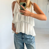 Kvinde iført hvid, lagdelt top og blå jeans tager spejlbillede med en grøn telefon. Hun står i et lyst rum, med én hånd i lommen og en gylden ring synlig.