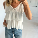 Kvinde iført hvid, flerlags top og blå jeans holder en smartphone, smiler og tager et spejlbillede. Håret er lys og skulderlangt, omgivet af et lyst interiør.