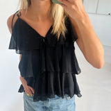 En person iført en sort, flæsebluse tager et spejlbillede, mens de holder en grøn telefon. De har også lyseblå jeans på. Rummet er lyst med hvide vægge.
