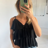 Kvinde står med en grøn telefon, dækker ansigtet, iført sort flæsetop og blå jeans, i et lyst rum med en hvid tavle i baggrunden.