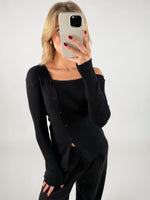 En person i sort trøje tager et selfie med en smartphone i et minimalistisk rum. Hendes hår er lyst, og hun har rød neglelak.