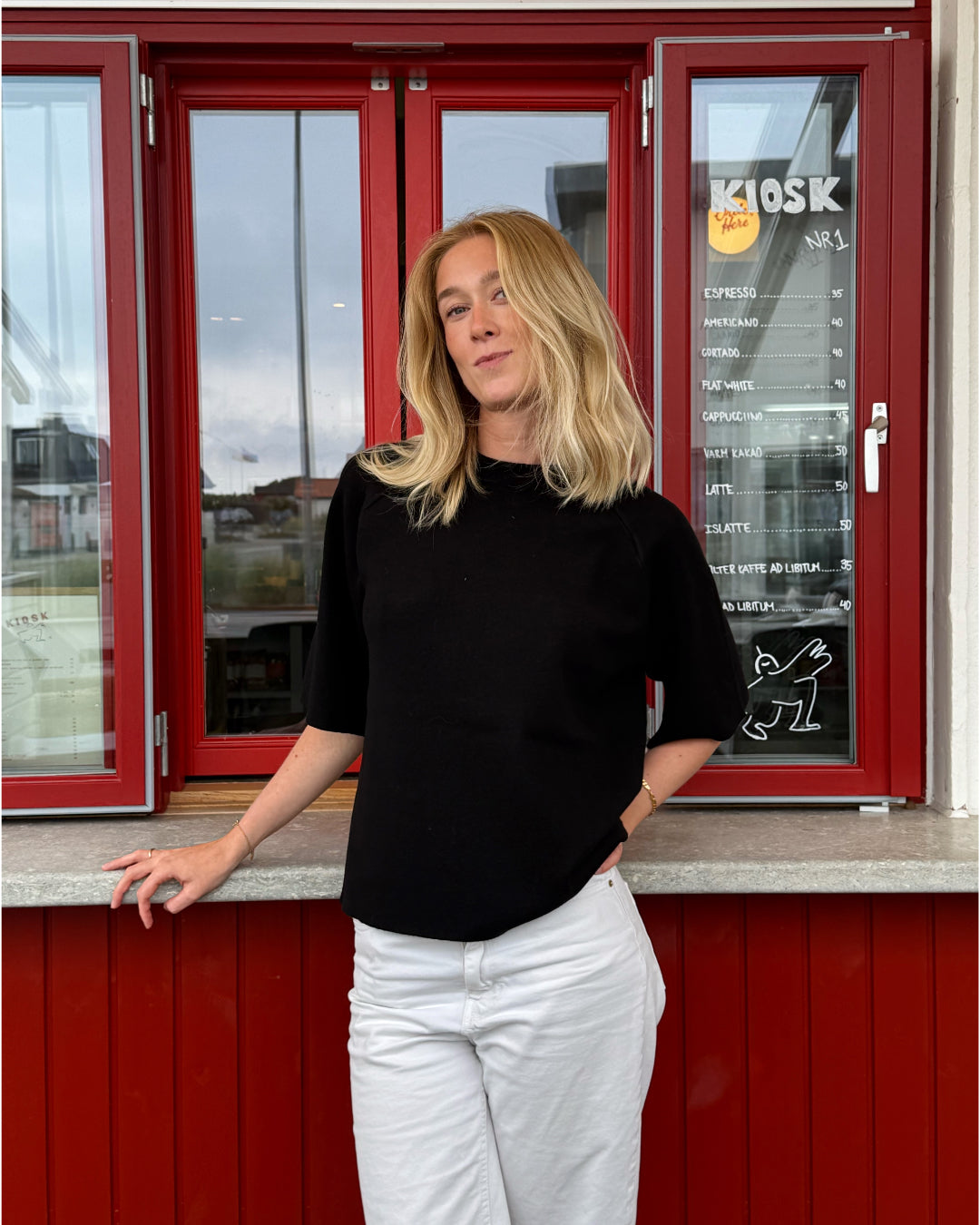 Modelfoto af pige der bærer Reynard strik t-shirt i sort, samt hvide bukser. Alt fra BySofieSønderby