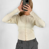 Modelfoto af pige i cremefarvet RORY striktrøje med knapper, samt grå LISA bukser. Alt er fra BySofieSønderby.