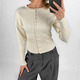 Modelfoto af pige i cremefarvet RORY striktrøje med knapper, samt grå LISA bukser. Alt er fra BySofieSønderby.