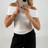 En person i en hvid top holder en mobiltelefon op foran ansigtet i en selfie-position, baggrund er neutral og lys.