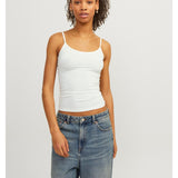 Person står stille iført en hvid tanktop og blå jeans i et minimalistisk, lysegråt rum.