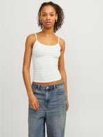 Person står stille iført en hvid tanktop og blå jeans i et minimalistisk, lysegråt rum.