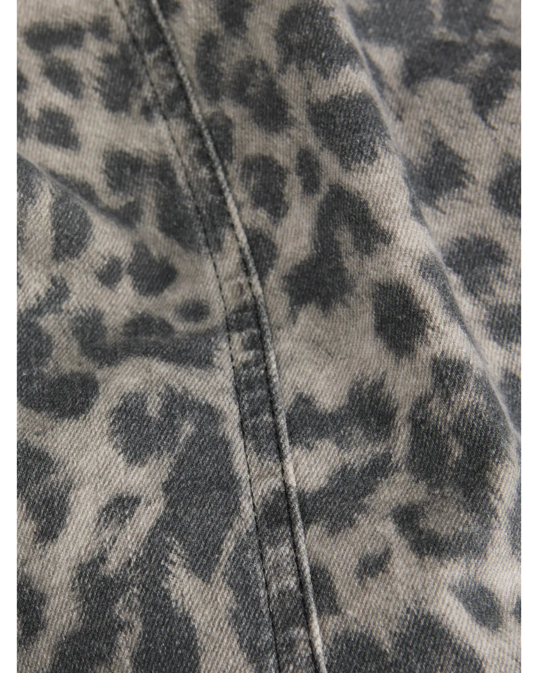 Grå og sort leopardmønstret stof ligger foldet med en synlig søm. Stoffet ser jævnt ud, hvilket tyder på tøj eller tekstil i blødt materiale.
