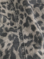 Grå og sort leopardmønstret stof ligger foldet med en synlig søm. Stoffet ser jævnt ud, hvilket tyder på tøj eller tekstil i blødt materiale.