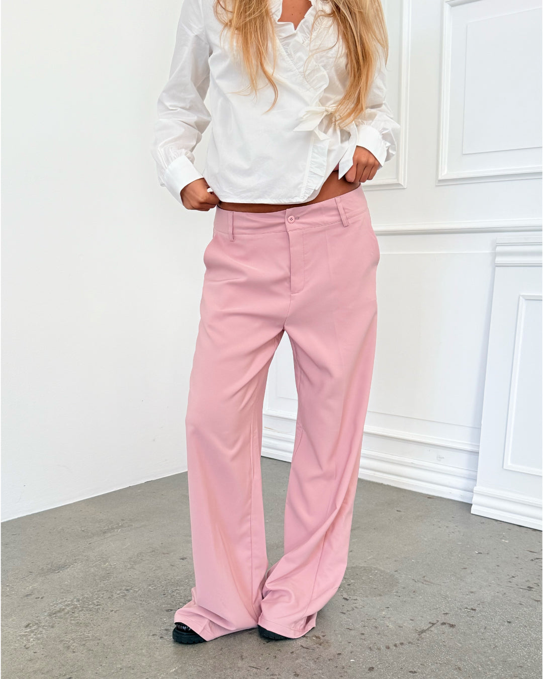 Modelfoto af pige i lyserøde SELENA bukser, samt hvid HOPE top. Alt er fra BySofieSønderby.