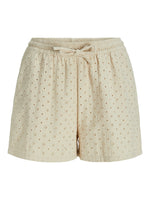 Shorts i blød beige stof, dekoreret med små broderede blomsterhuller, har en elastisk talje og bindebånd, synlig på en hvid baggrund.