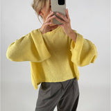 En person iført en gul sweater tager et billede med en telefon. Personen står i et neutralt rum og bærer grå bukser.