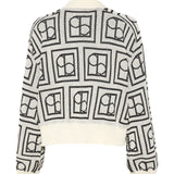 En hvid sweater med sort, geometrisk mønster bestående af kvadrater indeholdende cirkler og halve cirkler, ses mod en hvid baggrund.