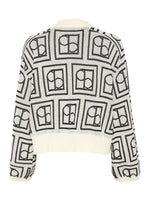 En hvid sweater med sort, geometrisk mønster bestående af kvadrater indeholdende cirkler og halve cirkler, ses mod en hvid baggrund.