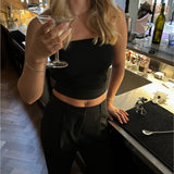 En kvinde i sort top holder et cocktailglas ved en bar. Detaljerede elementer som en flaske, glas og barudstyr er synlige i baggrunden.