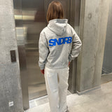 Stemningsbillede af pige der bærer en grå hoodie med blåt SNDRB tryk og hvide NANNA jeans.  Fra BySofieSønderby