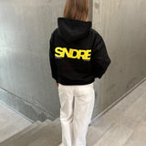 Stemningsbillede af pige der bærer en sort hoodie med gult SNDRB tryk og hvide NANNA jeans.  Fra BySofieSønderby