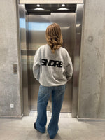 Stemningsbillede af pige der bærer en grå sweatshirt med sort SNDRB tryk og blå NANNA jeans.  Fra BySofieSønderby