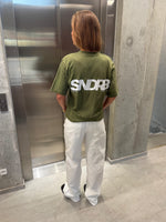 Stemningsbillede af pige der bærer en army t-shirt med hvidt SNDRB tryk og hvide NANNA jeans.  Fra BySofieSønderby