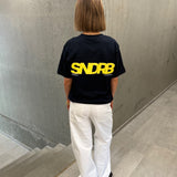 Stemningsbillede af pige der bærer en navy t-shirt med gul SNDRB tryk og hvide NANNA jeans.  Fra BySofieSønderby