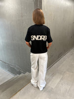 Stemningsbillede af pige der bærer en sort t-shirt med beige SNDRB tryk og hvide NANNA jeans.  Fra BySofieSønderby