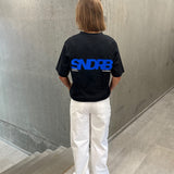 Stemningsbillede af pige der bærer en sort t-shirt med blå SNDRB tryk og hvide NANNA jeans.  Fra BySofieSønderby