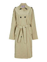 Beige trenchcoat hænger, med bælte bundet i taljen, sorte knapper og skulderstropper, mod en hvid baggrund.